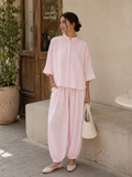 Woman in a pink outfit standing outdoors near a building entrance.