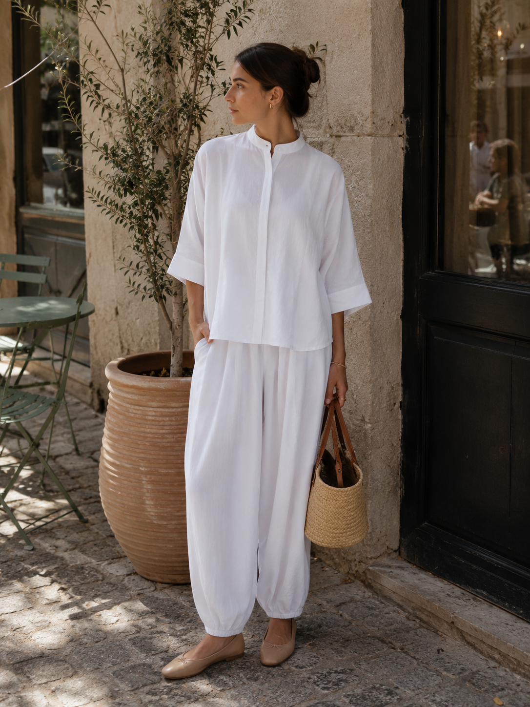 Woman in a white outfit standing outdoors near a building entrance.