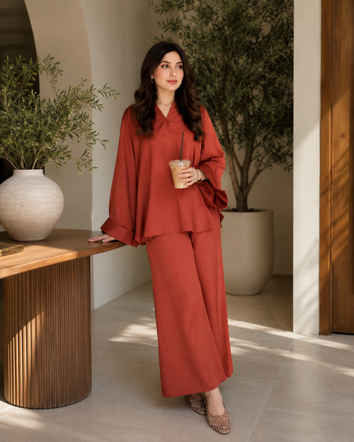 Woman in a rustyoutfit holding a coffee in a modern indoor setting