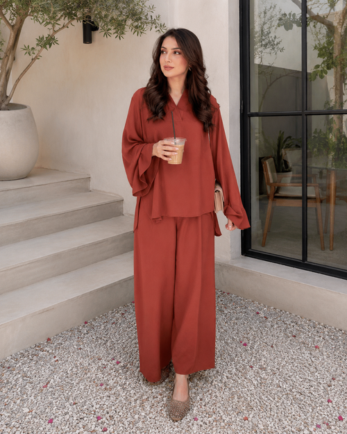 Woman in a rust-colored outfit standing outdoors holding a drink.